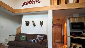 Ein geräumiger Wohnbereich mit einem braunen Sofa, einer Holztreppe und einer Küchenzeile.