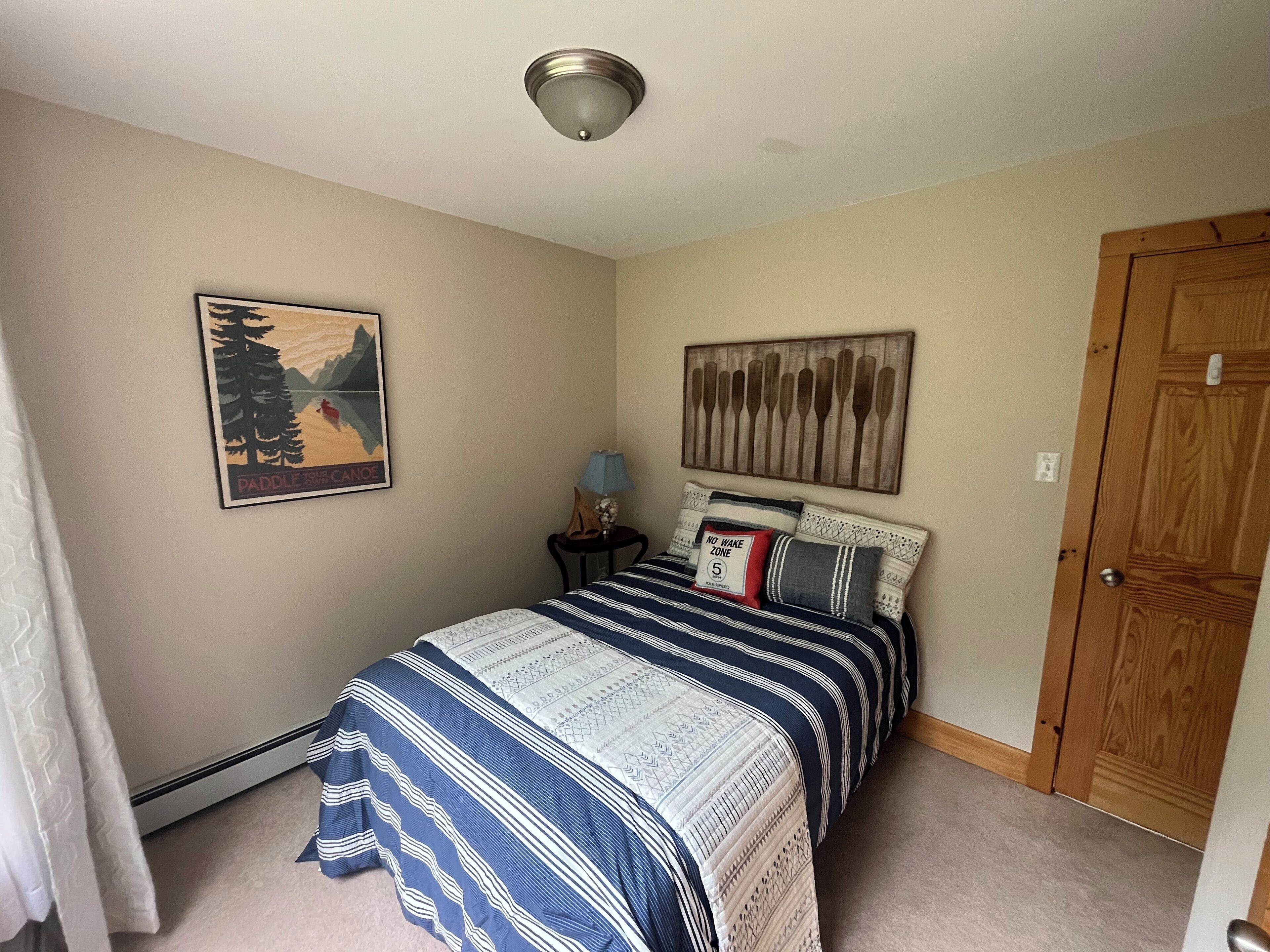 A bedroom with a bed, a nightstand, a lamp, a door, and two wall decorations.