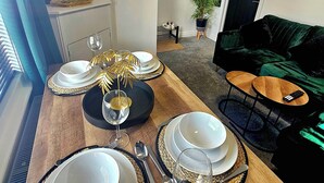 Un'area pranzo con tavolo in legno apparecchiato per quattro persone, con piatti, bicchieri, posate e un elemento decorativo al centro.