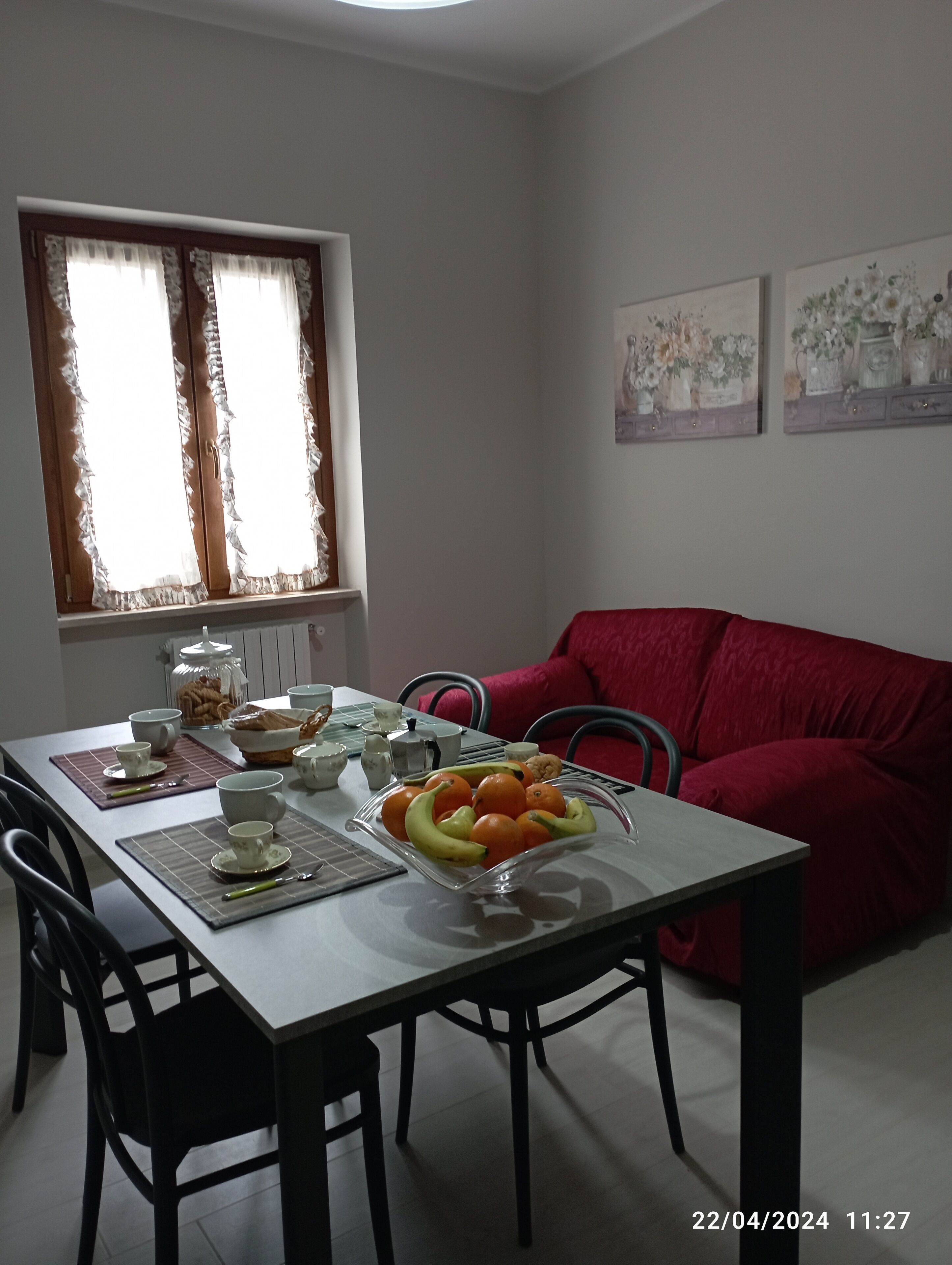 A dining area with a table set for four, a red sofa, and two windows with curtains.