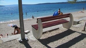 Une plage avec un banc en bois, des gens qui prennent un bain de soleil et une mer calme.