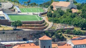 Une ville côtière dotée d’une muraille fortifiée, d’une église et d’un terrain de sport.