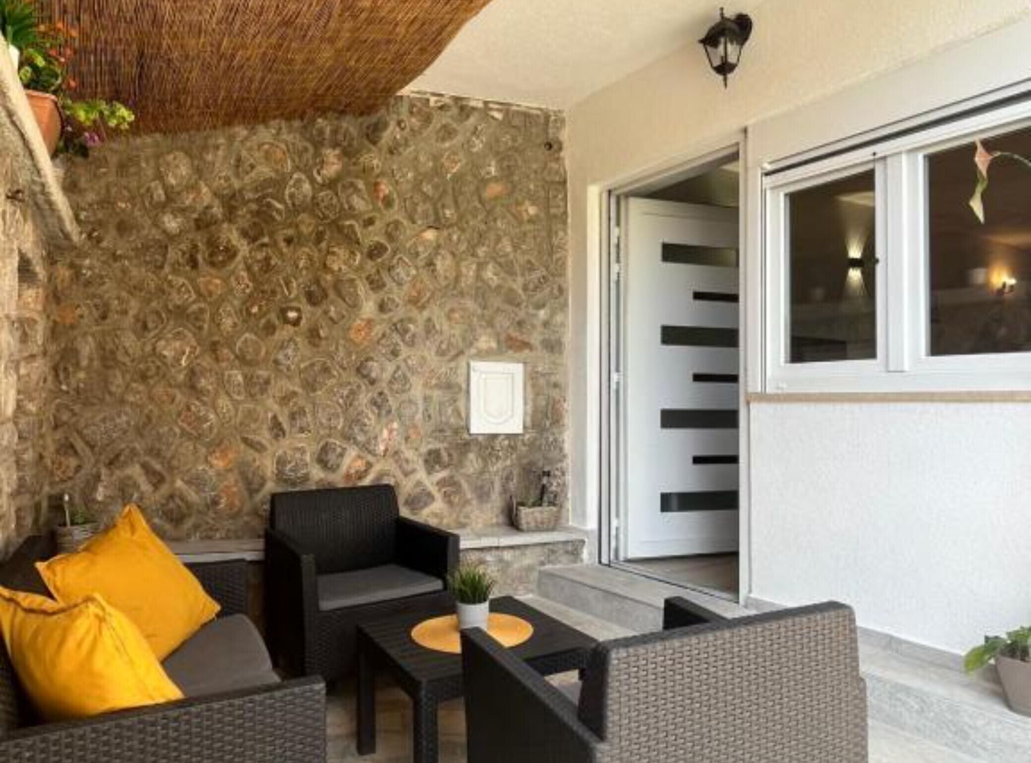 A patio area with wicker furniture, a stone wall, and a sliding glass door leading to an interior space.