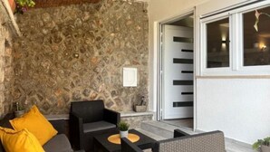 Un espace extérieur aménagé en terrasse, avec des meubles en osier, un mur en pierre et une porte-fenêtre coulissante donnant sur un espace intérieur.
