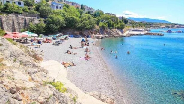 Une plage avec une eau d’un bleu limpide, des gens qui prennent des bains de soleil et des parasols.