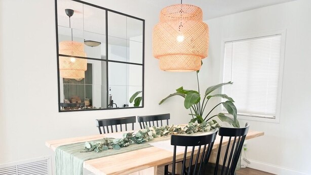 A dining area with a wooden table, black chairs, a large mirror, and a hanging orange pendant light. - Resort Style Home Near Universal/Disney (Orlando)