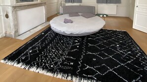 Un dormitorio moderno con una cama redonda, una alfombra estampada en blanco y negro, una lámpara de techo y un espejo grande.