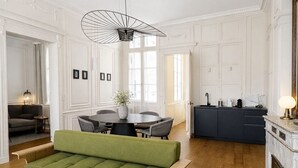 Un amplio salón con un sofá verde, una mesa redonda de centro y una mesa de comedor con sillas.