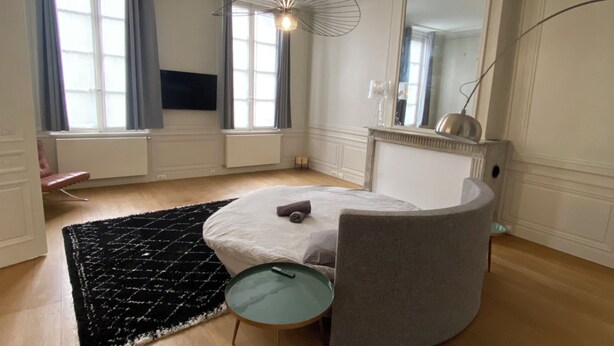 Un dormitorio moderno con cama redonda, una mesita auxiliar pequeña, un espejo grande y una lámpara de techo original.