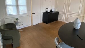 Una habitación amplia con una mesa de comedor redonda, dos sillas, una pequeña mesita con una planta y una zona de cocina con encimera y armarios negros.
