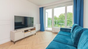 Un saló modern amb televisió de pantalla plana sobre un moble blanc, un sofà blau i una finestra gran amb cortines blaves.