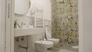 Un baño moderno con inodoro, bidé y lavamanos. Hay un perchero sobre el lavamanos y una ducha con cortina de motivos de hojas.