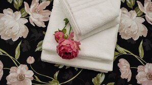 Una toalla blanca doblada con un rosal rosa encima, sobre un fondo estampado con flores.