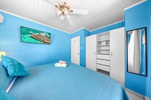 Une chambre à coucher avec un lit, un ventilateur de plafond, une armoire et un tableau au mur.