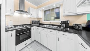 Una cocina moderna con armarios blancos, encimera negra, estufa, microondas, lavaplatos y ventana.