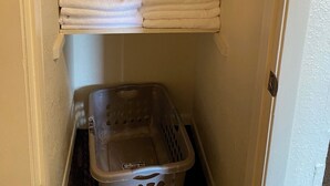 A storage closet with shelves holding folded towels and a laundry basket.