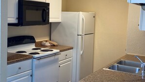 A compact kitchen with white cabinets, a black microwave, a white refrigerator, a stove with four burners, and a granite countertop.
