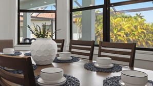 Une table à manger avec de l’assiette et des bols blancs, un vase blanc orné de verdure et des chaises en bois.