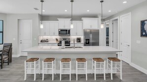 Une cuisine moderne avec des meubles blancs, un grand îlot central doté de tabourets, des appareils en acier inoxydable et un éclairage suspendu.