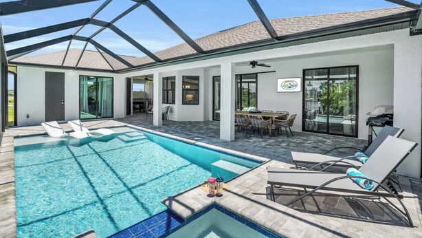 Un espace piscine intérieur moderne, avec une eau d’un bleu limpide, des chaises longues et un patio couvert comprenant une table et des chaises pour prendre les repas.