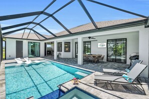 A modern indoor pool area with clear blue water, lounge chairs, and a covered patio with a dining table and chairs. - Luxe-Boat Rental, MIL Suite, Kayaks, Bikes, Park (Cape Coral)