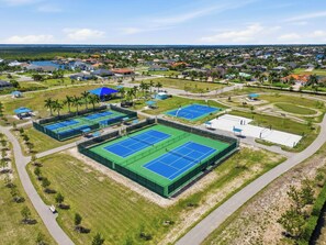 Luchtbeeld van een woongebied met meerdere tennisbanen, een park en een waterpartij op de achtergrond.