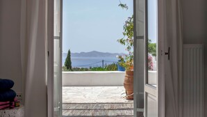 Une porte ouverte donnant sur un balcon avec vue sur la mer et les montagnes.