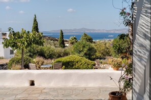 A terrace with a view of the sea and mountains, featuring a white wall, potted plants, and outdoor furniture. - Sea-View Cycladic Villa near Alyki – Family Home with Olive Garden & Starlink (Paros)