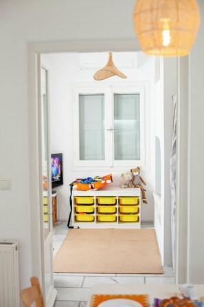 A child's room with a window, a small table with toys, and storage bins. - Sea-View Cycladic Villa near Alyki – Family Home with Olive Garden & Starlink (Paros)