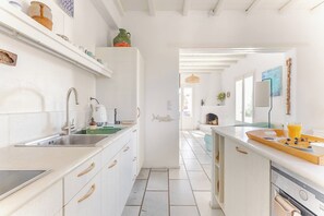 A kitchen with white cabinetry, a built-in dishwasher, and a breakfast setup with a cutting board and a glass of orange juice. - Sea-View Cycladic Villa near Alyki – Family Home with Olive Garden & Starlink (Paros)
