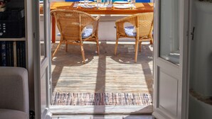 Une porte ouverte donne sur un coin repas aménagé avec des meubles en osier et un luminaire suspendu au plafond, fait de matériaux tressés.
