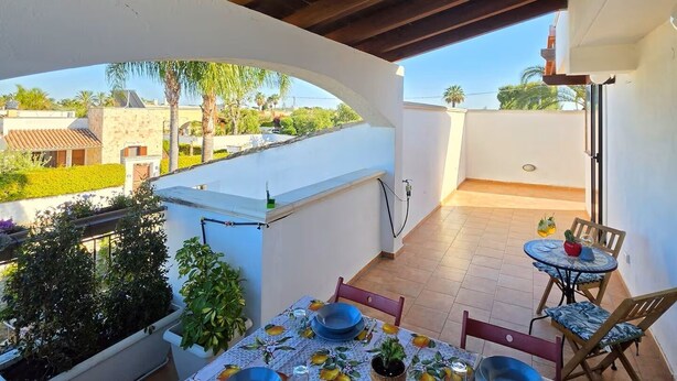Une terrasse extérieure avec une table dressée pour le repas, entourée de plantes en pot et offrant une vue sur le quartier.