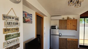 Une cuisine moderne avec des meubles en bois, un réfrigérateur en acier inoxydable et un four à micro-ondes. On y trouve également un téléviseur posé sur un meuble en bois et une horloge murale.