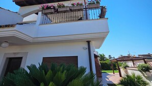 Un immeuble de deux étages doté d’un balcon orné de fleurs roses, d’une façade blanche et surplombant un ciel d’un bleu limpide.