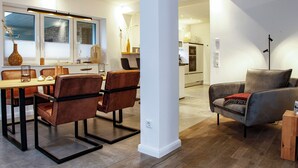 Een moderne woonkamer met een eethoek, met een bank, stoelen en een salontafel.