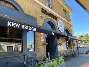 A building with a sign reading "KEW BRIDGE" and another sign for "The Roastery." - New Spacious 4 Bed Apartment in Kew Bridge (Brentford)