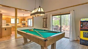 A pool table in a room with wooden flooring, a hanging lamp, and a view of an outdoor area through a glass door. - Steps2Lake, BonusLoft, 2 full Baths, 7Beds, Pool Table, 2 Kayaks, 2 Arcade Games (Pocono Lake)