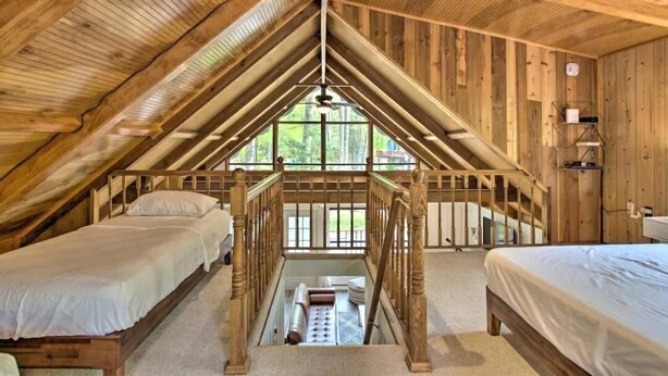 A cozy attic bedroom with wooden beams, a central staircase, and two beds. - Steps2Lake, BonusLoft, 2 full Baths, 7Beds, Pool Table, 2 Kayaks, 2 Arcade Games (Pocono Lake)