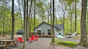 A cabin with a deck, surrounded by trees, and a hammock. - Steps2Lake, BonusLoft, 2 full Baths, 7Beds, Pool Table, 2 Kayaks, 2 Arcade Games (Pocono Lake)