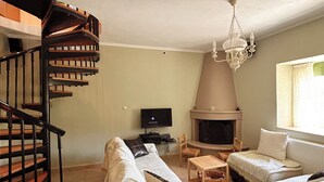 A living room with a spiral staircase, a fireplace, a television, and two beds.