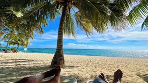 A beach scene with a palm tree, clear blue sky, and calm sea. - Waterfront Sanctuary Grande 4Bed 4Bath Pool Patio (Grand Harbour)
