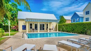 A pool area with lounge chairs, a covered seating area, and a building with a sign. - Waterfront Sanctuary Grande 4Bed 4Bath Pool Patio (Grand Harbour)