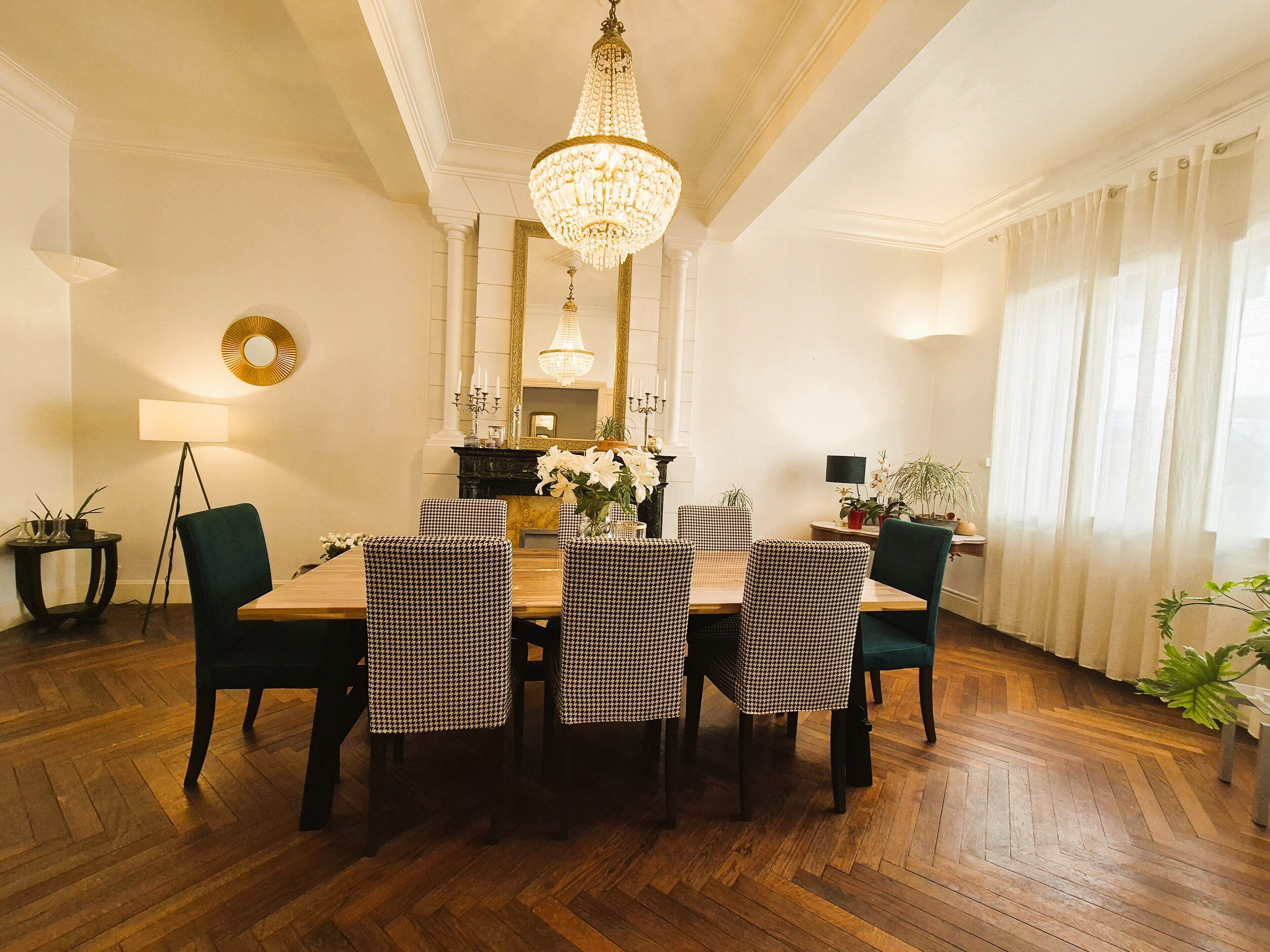 A dining area with a wooden table, houndstooth chairs, a chandelier, and a piano.