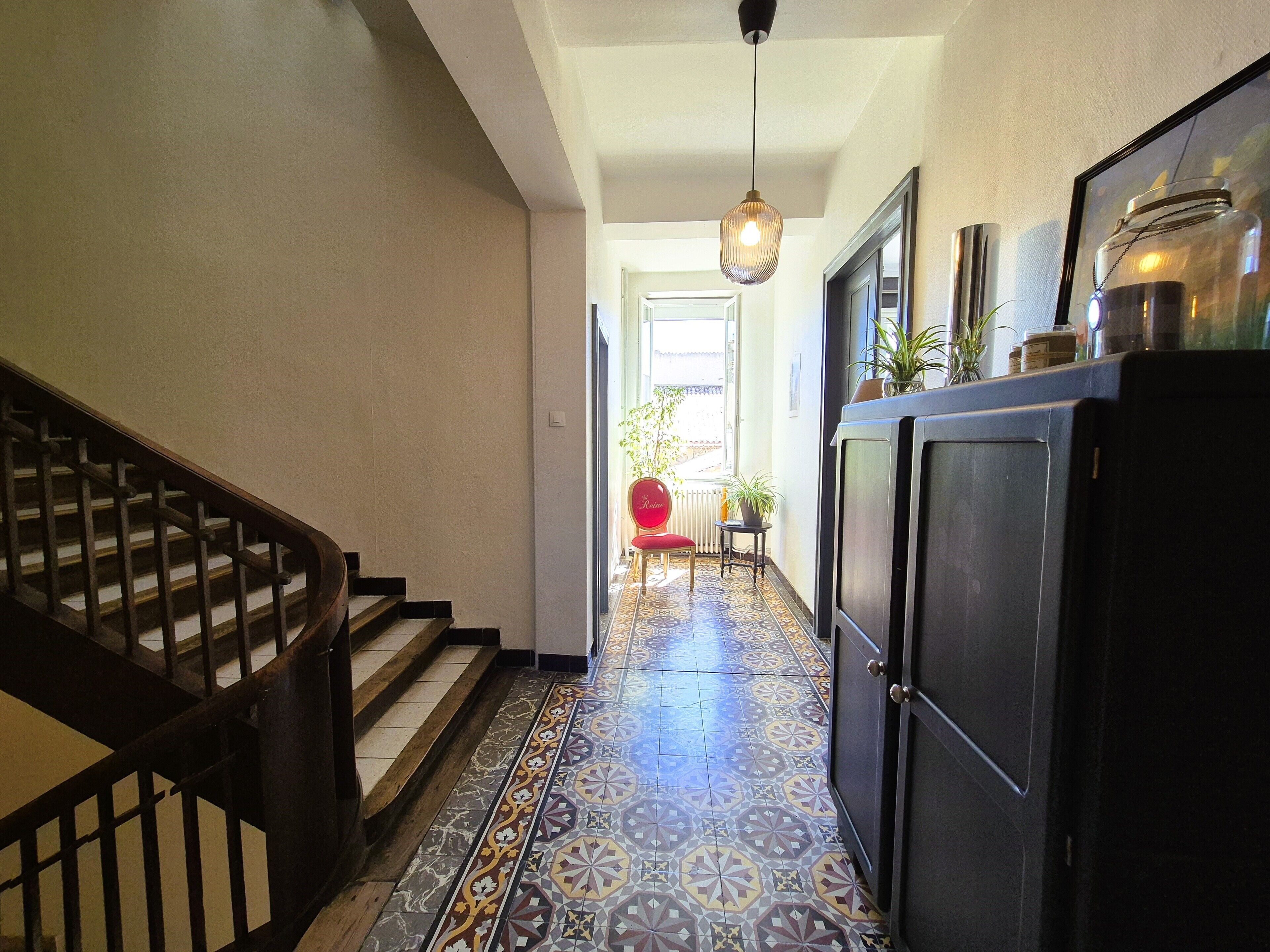 Un couloir doté d’un sol à motifs, d’un escalier, d’une armoire et d’un luminaire suspendu.