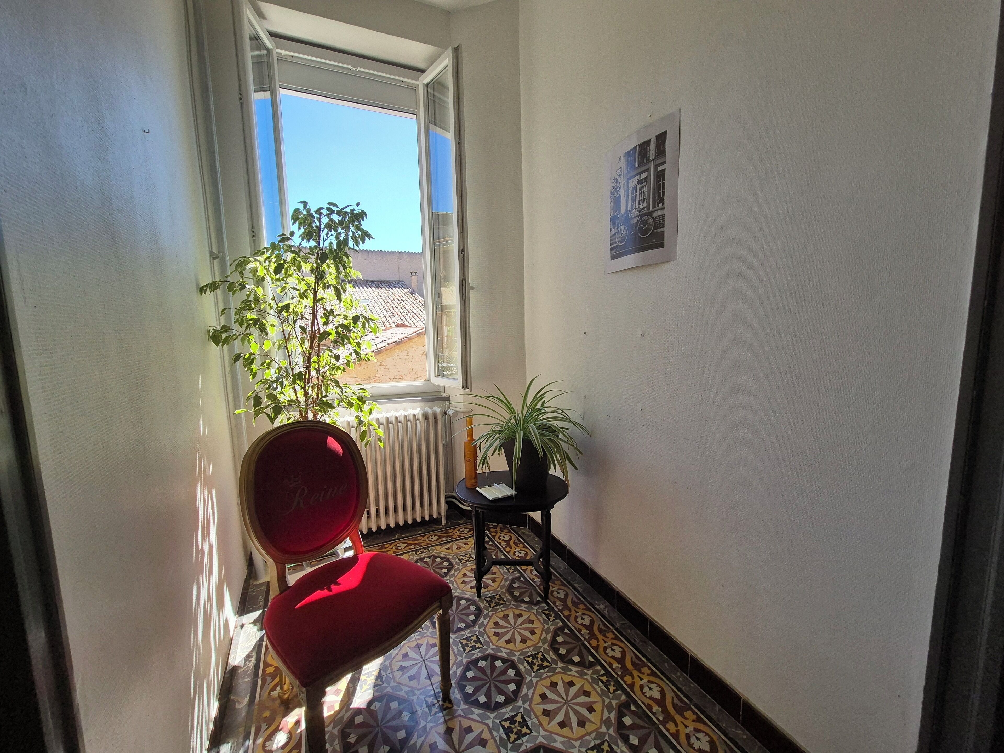 A narrow hallway with a red chair, a potted plant, and a radiator.