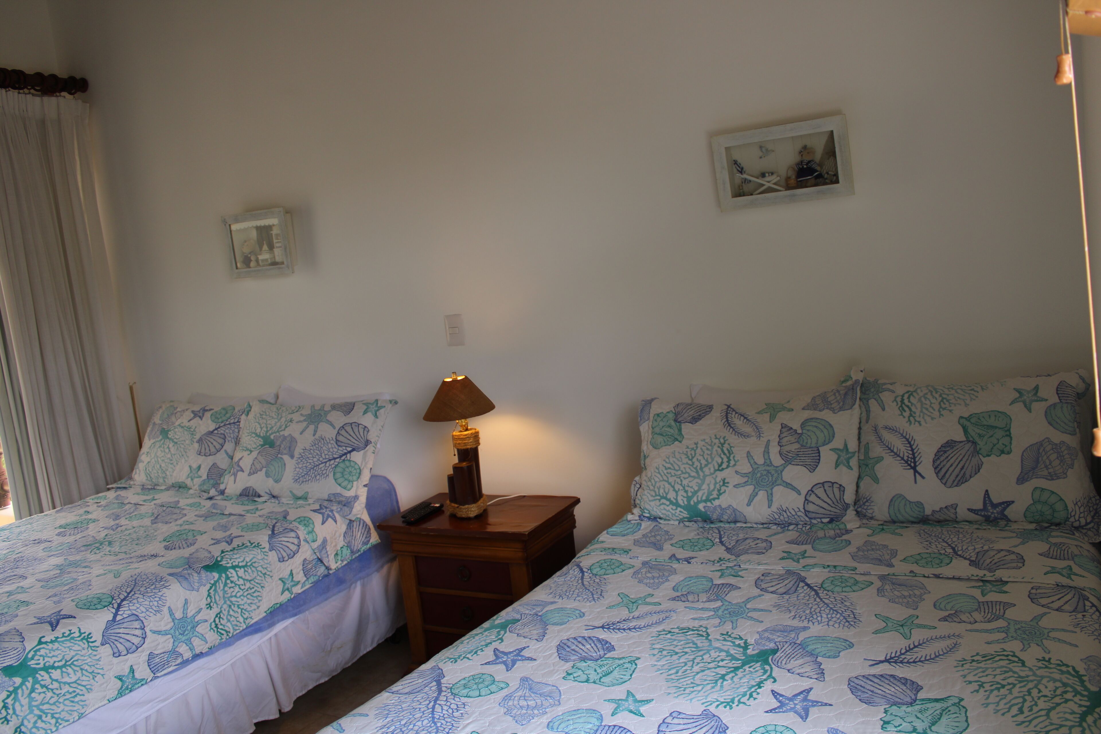 Una camera da letto con due letti, ognuno con copriletto a tema marino, un comodino con una lampada e un piccolo quadro appeso alla parete.