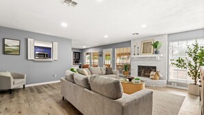 Ein modernes Wohnzimmer mit einer grauen Couch, einem Kamin und einer Küche im Hintergrund.