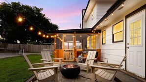 Eine Terrasse im Freien mit vier Adirondack-Stühlen, einer Feuerstelle und Lichterketten.