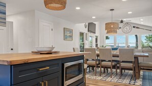 Cocina moderna con encimera de madera, horno integrado y muebles negros. Cuenta con un comedor con mesa y sillas, y vistas al exterior a través de amplias ventanas.