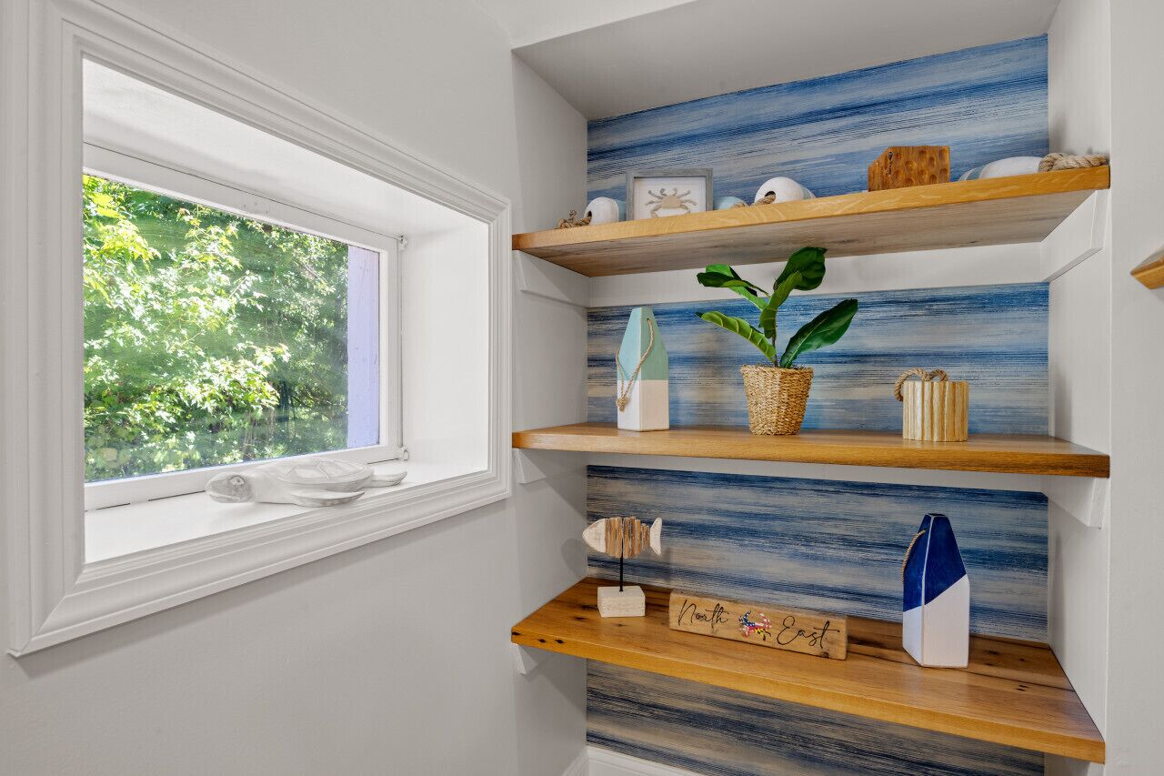 A room with a window, wooden shelves with decorative items, and a wall with a blue and white pattern.